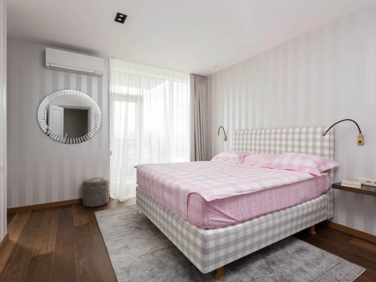 Modern bedroom with a wall-mounted air conditioning unit above a round wall mirror